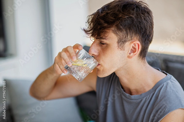 Obraz Young man drinking water with lemon from a glass on the sofa at home close-up