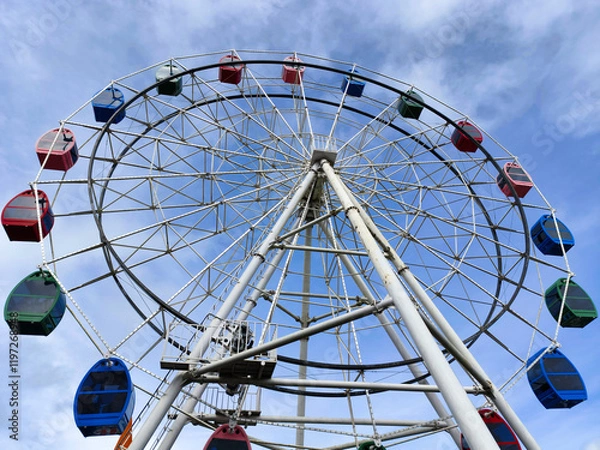 Fototapeta Colorful Ferris Wheel Against Bright Blue Sky in Amusement Park Setting