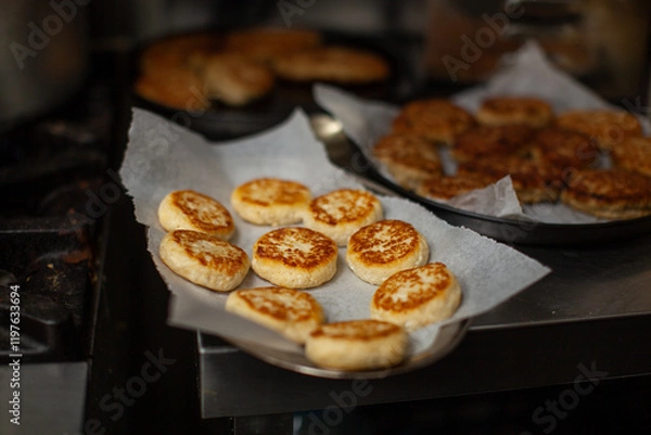 Fototapeta Delicious syrniki cooling on baking paper after being cooked on a pan in a professional kitchen