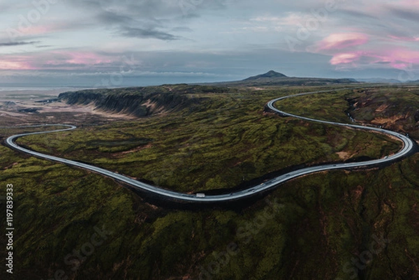 Fototapeta Aerial view of Iceland's Route 1 winding through Hellisheidi, surrounded by vibrant volcanic landscapes at sunrise.