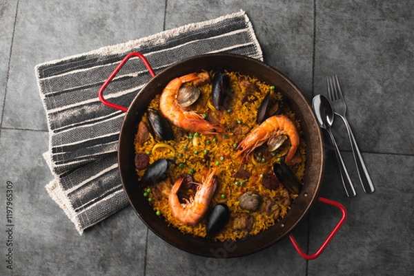 Fototapeta Classic Spanish dishes, seafood paella in a traditional skillet against the rustic blue concrete backdrop. Spanish paella with shrimp, hugs, mussels, green peas, and fresh lemon wedges from above.