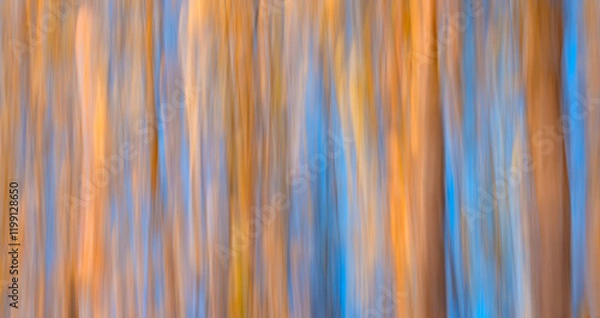 Fototapeta image is a blurry, abstract painting of trees with a blue and orange background. The colors and brushstrokes create a sense of movement and energy, as if the trees are swaying in the wind