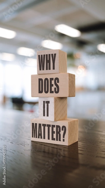Obraz Stacked wooden blocks on a dark surface spell "WHY DOES IT MATTER?" in dark brown sans-serif font. A blurred, bright interior background emphasizes the clean, reflective design.







