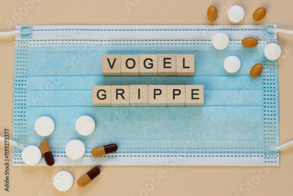 Fototapeta Vogelgrippe - avian influenza in German, spelled with wooden cubes on a surgical mask with scattered pills around.
