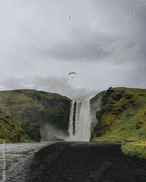 Fototapeta Skógafoss waterfall in South Iceland with a paraglider soaring above...