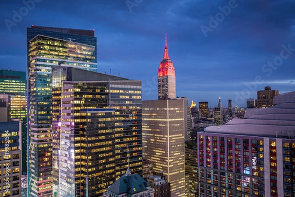Fototapeta A nighttime view of Manhattan downtown in the New York City showcasing illuminated skyscrapers, set against a deep blue sky.