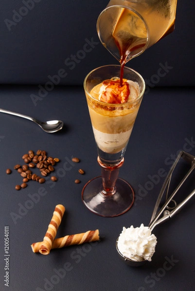 Fototapeta serving an italian coffee affogato in a tall glass cup on a dark blue background with coffee beans, ice cream scoop and spoon