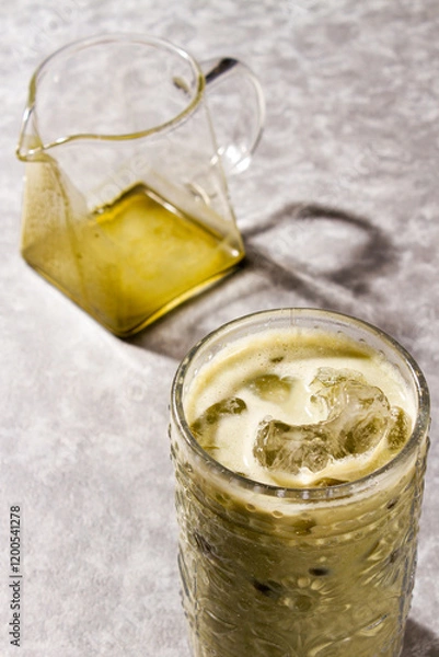 Fototapeta Iced Matcha Latte served into cold glass with ice, an empty glass jar over a grey background