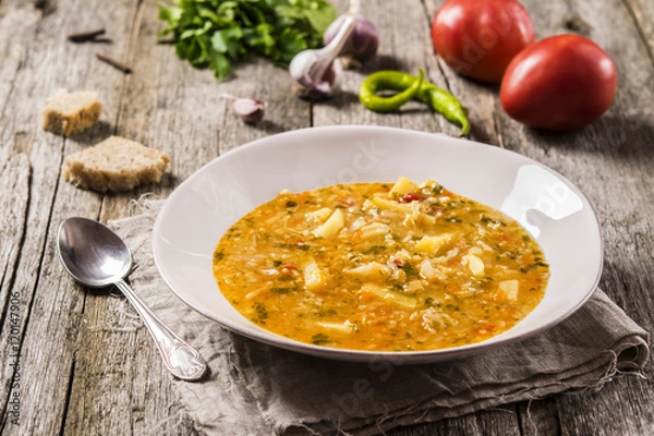 Fototapeta Vegetarian vegetable soup with potatoes, cabbage, tomatoes, peppers and millet on the rough wooden background. Selective focus 