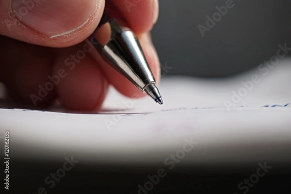 Fototapeta Male hand holding a sharp blue office pen and writing to the white lined notepad as a symbol of taking notes or business communication 