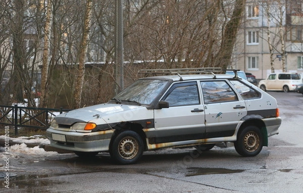 Fototapeta An old rusty silver car is parked in the courtyard of an apartment building, Iskrovsky Prospekt, Saint Petersburg, Russia, January 17, 2025