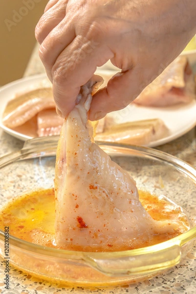Fototapeta Chef dips a piece of fish into liaison - a mixture of raw eggs, salt, paprika before frying