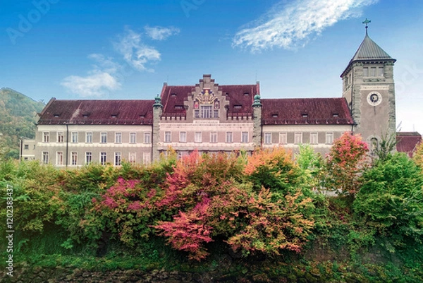 Fototapeta Historic clock tower building in Feldkirch, Austria surrounded by vibrant autumn foliage, picturesque mountain backdrop, and classic European architecture showcasing timeless beauty