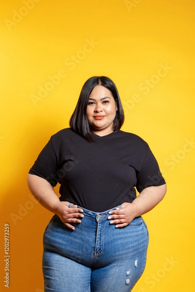 Fototapeta Plus size woman posing with hands on hips on yellow background