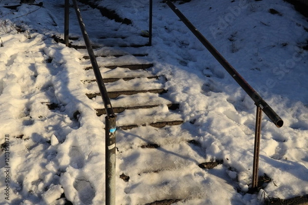 Fototapeta Winter staircase with handrails and steps under snow and ice illuminated by the sun