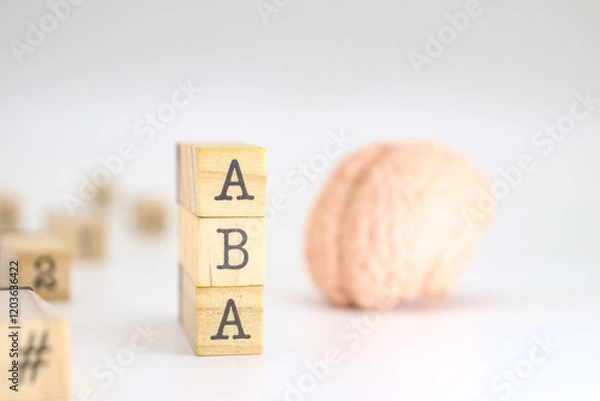 Obraz Applied behavior analysis acronym. ABA written on wooden cubes isolated with a figure of a brain on white background with space for text.