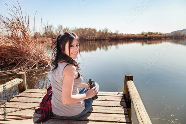 Obraz Young woman sitting on the pier smiling while looking back at the camera