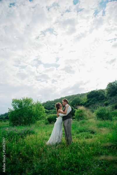 Fototapeta the bride and groom with a bouquet in the grass against the background mountain landscape