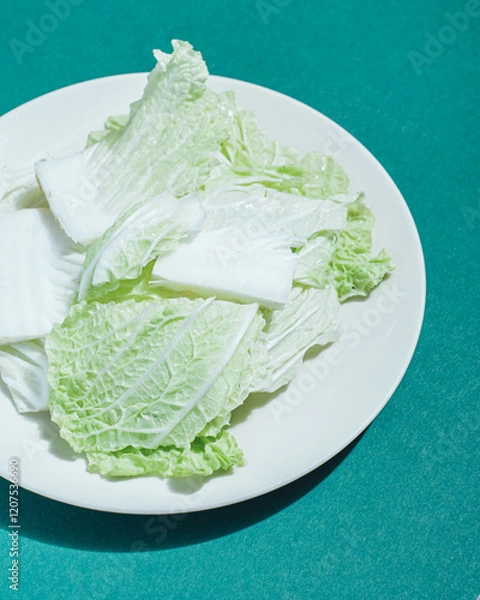 Fototapeta pieces of fresh iceberg lettuce on a white plate on a green background with hard shadow