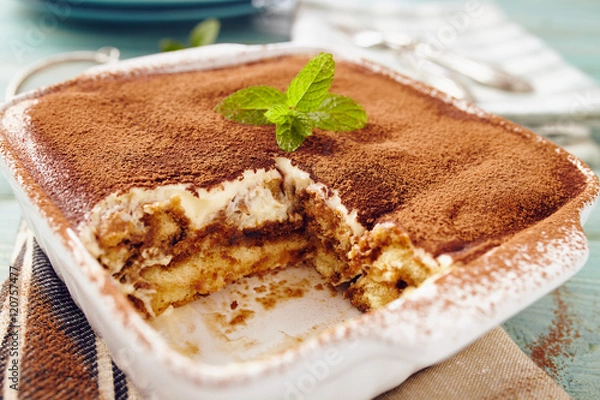 Obraz Tiramisu cake in an oven pan on a blue wooden  table with dishes and forks