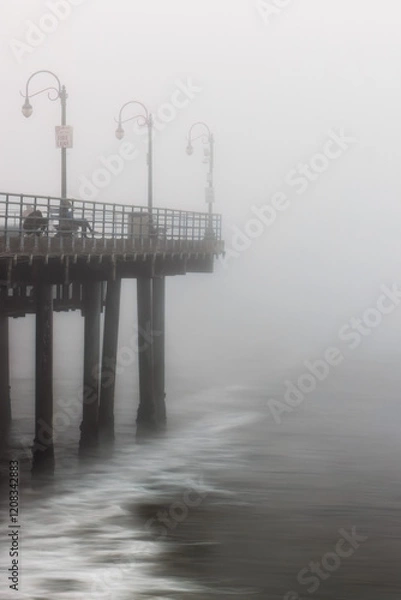 Fototapeta A pier in Santa Monica, California, covered in fog, with the waves crashing on shore.
