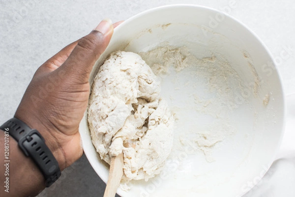 Fototapeta Overhead view of bread dough being mixed in a white bowl, top view of homemade bread dough being mixed on white granite countertop, process of making artisan bread