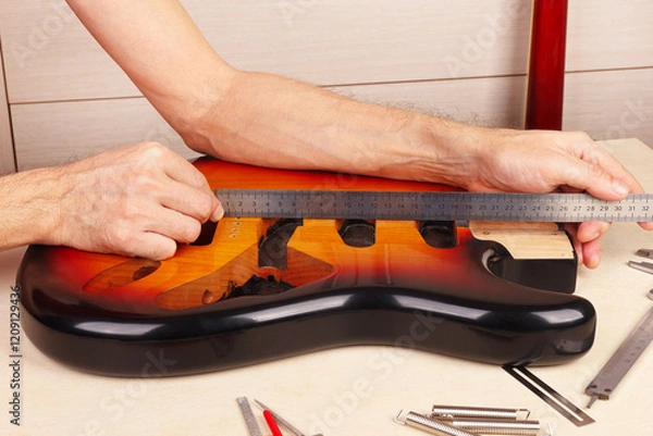 Obraz Guitar repairer measures body of guitar with ruler.