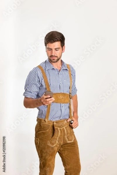 Obraz Junger Mann in Lederhose bedient sein Handy