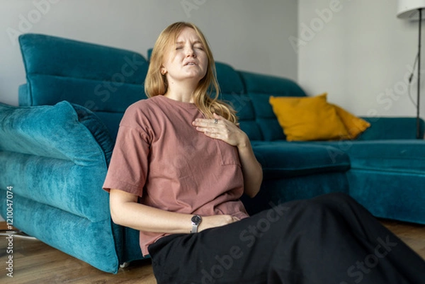 Fototapeta Woman sitting with strong chest pain and hand touching her chest while having trouble at home. Heart attack concept or heart failure symptom. Pressure in the chest.