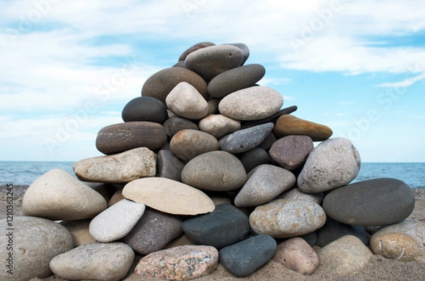 Fototapeta Triangular pile of stones stacked in foreground with blue sky white cloud background on beach