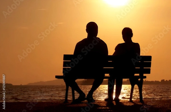 Fototapeta Couple in silhouette seated on a bench in contemplation in front of a lake at sunset. Quiet and peaceful Valentine day moment