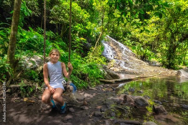 Fototapeta A child happily sits on a swing, playfully enjoying the moment near a serene tropical waterfall, surrounded by lush greenery and the beauty of nature all around, Tumpak Sewu waterfall, Java, Indonesia