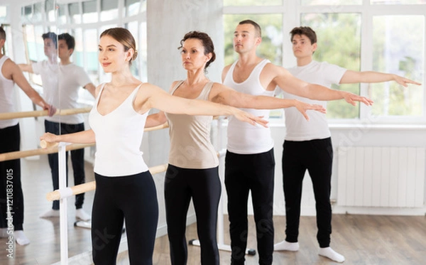Fototapeta Group of male and female dancers stand in second ballet pose at barre in dance class