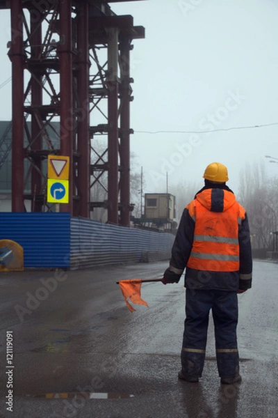 Obraz Worker in uniform with flag standing across the road preventing traffic in the construction area