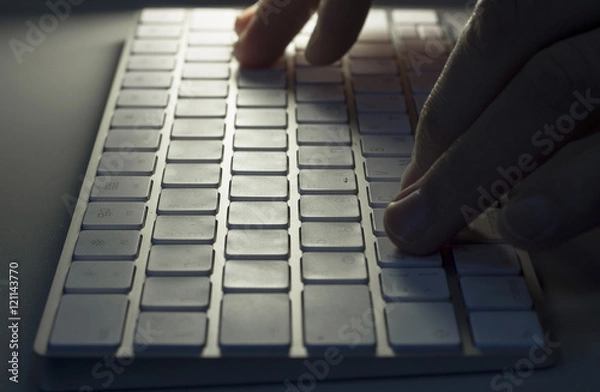 Obraz Male hands typing on white computer keyboard, close-up, in the dark