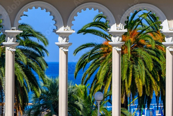 Obraz Columns against the background of tropical palm trees of the colonnade in Gagra in Abkhazia offer a beautiful view of the Black Sea coast. Trip, travel on vacation.