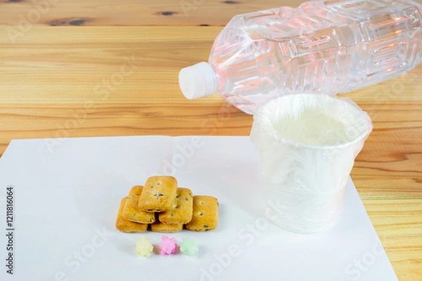 Fototapeta ビニール袋でカバーされた水が入った紙コップと避難所配給品の一食分の乾パン