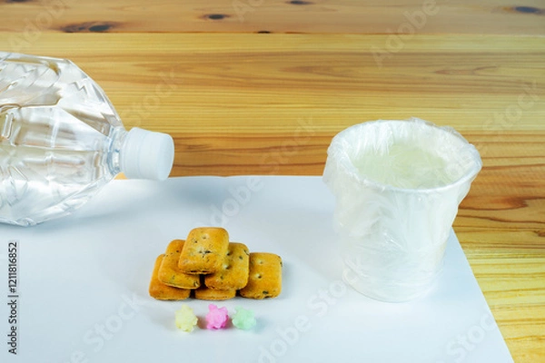 Obraz ビニール袋でカバーされた水が入った紙コップと避難所配給品の一食分の乾パン