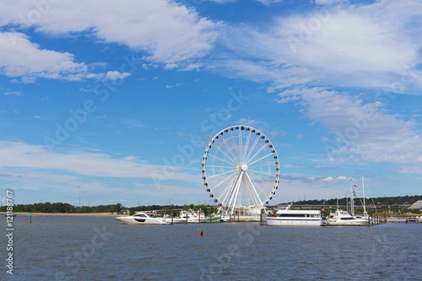 Fototapeta Ferris of National Harbor in Oxon Hill, Maryland, USA. Boats and yachts at National Harbor pier on a bright sunny day.