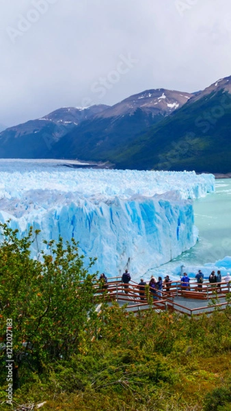 Fototapeta Vertical image of Perito Moreno. Tourists standing at the viewpoint looking a the edge of the Perito Moreno glacier.  Los Glaciares National Park