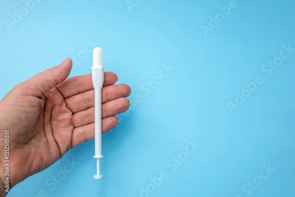 Fototapeta Vaginal tablet and applicator in hand on blue background. Close up. Place for text. Caring for women's health.