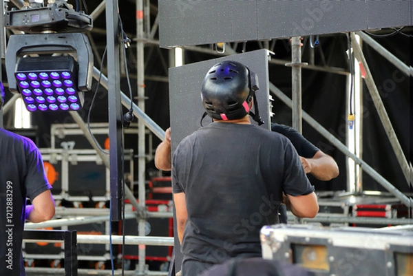 Fototapeta Technicians working on stage assembling giant LED screen panels for rock event. Men working on music show production.