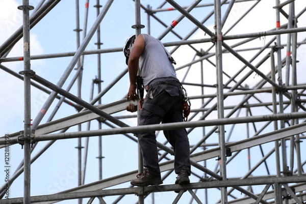 Fototapeta 
Construction worker in safety clothing setting up scaffolding for a stage or construction site