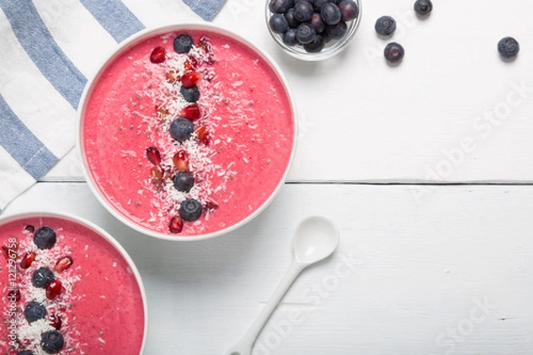 Fototapeta Strawberry and beetroot smoothie bowls topped with blueberries, pomegranate seeds and shredded coconut on a white wooden table. Top view with copy space