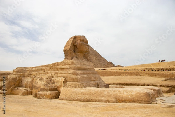 Fototapeta Historically known statue called Sfinx with face of human, body of lion and Cheop's pyramid in the background.