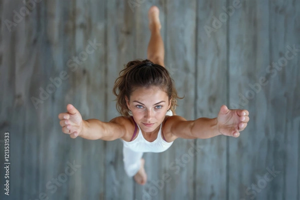 Obraz Woman performing yoga warrior crescent lunge pose with precision and strength, captured from above on rustic wooden floor