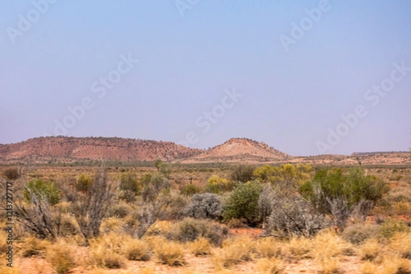 Obraz Rocky hills behind a treeless dry savannah landcape with dry grass and scrub  near Erldunda in the Norther Territory of Australia