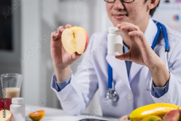Fototapeta A male nutritionist working at a hospital desk, holding an apple and mixed fruit, offering care, health advice, weight loss guidance, and eating tips online for patients seeking nutrition support