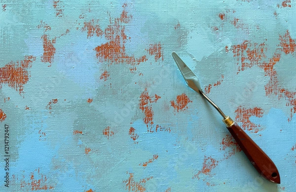 Fototapeta Palette knife on a painting canvas. The artist's metal tool with a wooden brown handle, with blue paint, lies on a canvas with an abstract acrylic painting.
