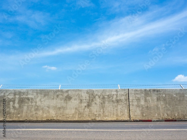 Fototapeta Concrete wall street with barbed wire fence under a blue sky and